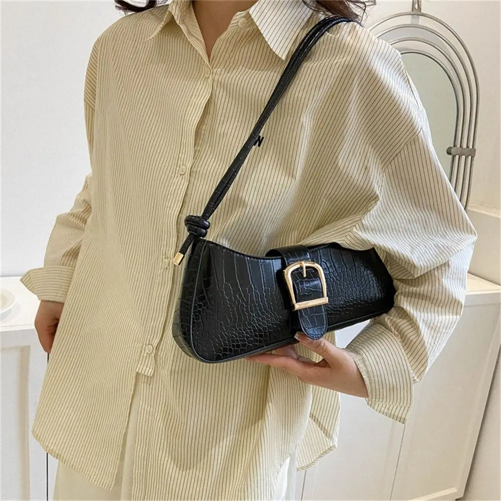 Person wearing a beige shirt holding a black handbag with a gold buckle.
