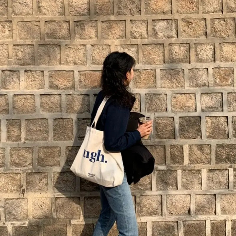 Person holding a tote bag with text against a brick wall