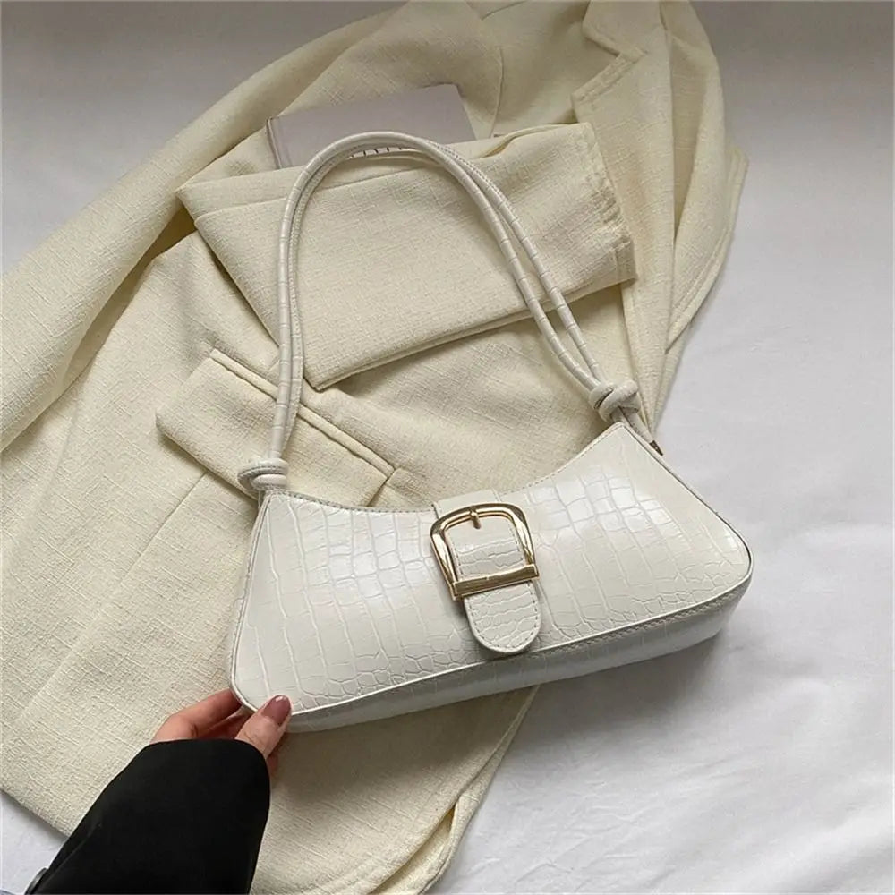White handbag with gold buckle held by a hand against a light background