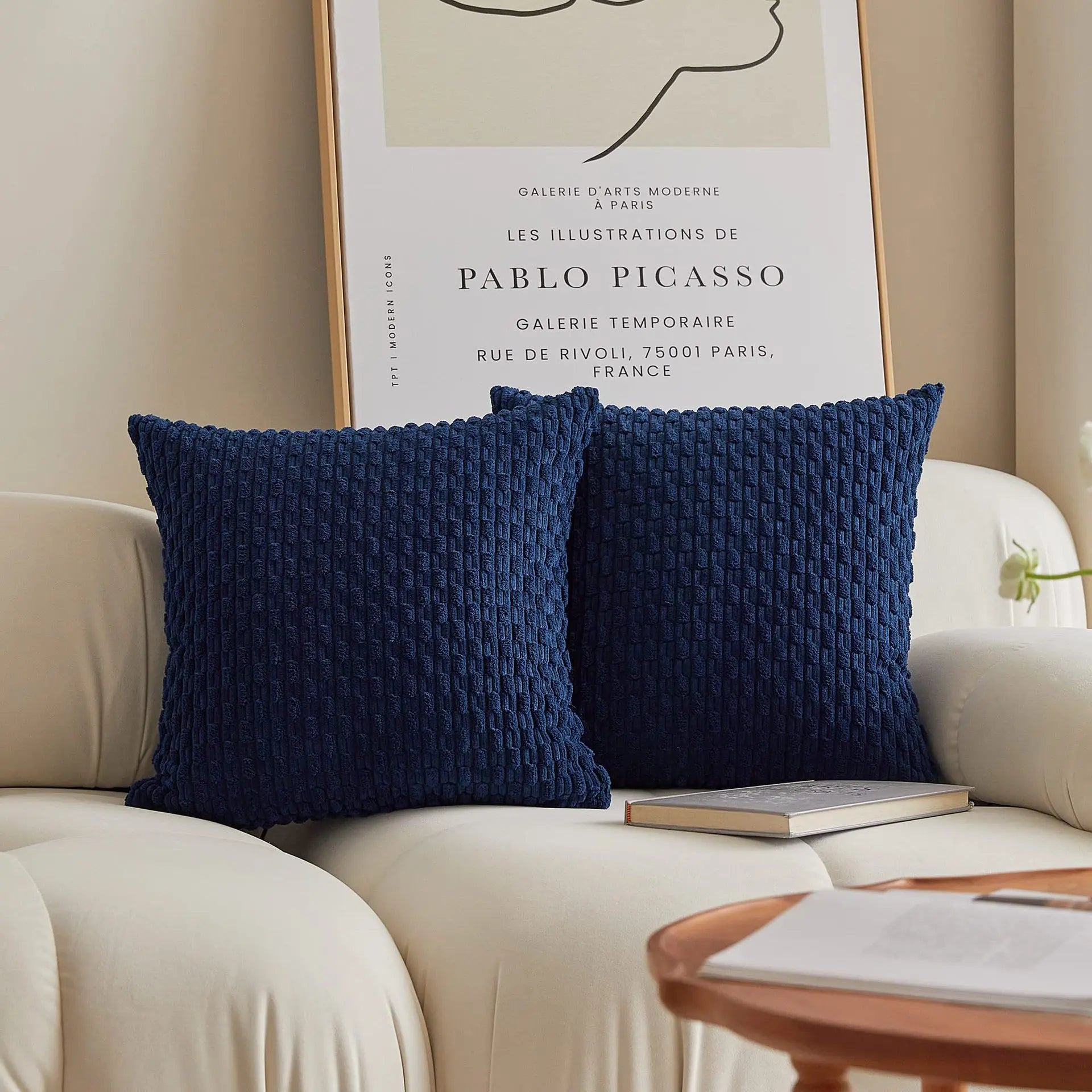 Two blue textured pillows on a beige sofa with a Picasso poster in the background.