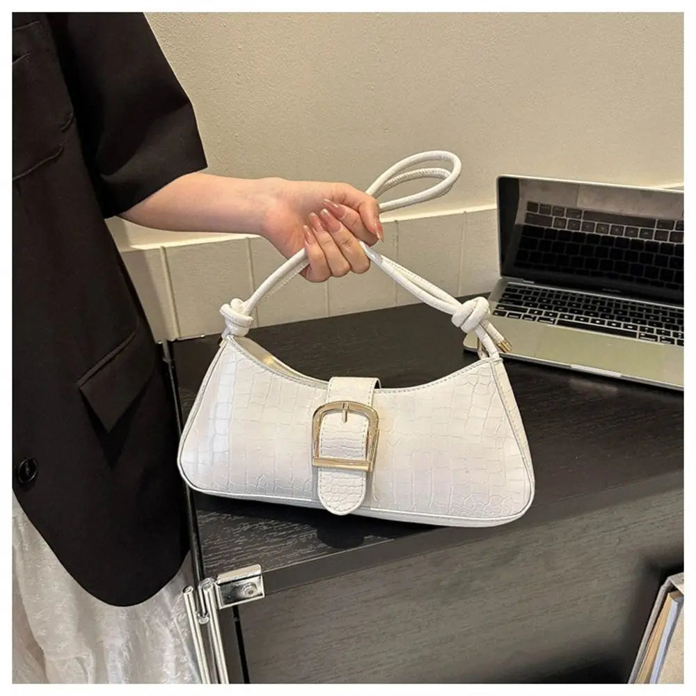White handbag with a silver buckle held by a person next to a laptop on a desk.