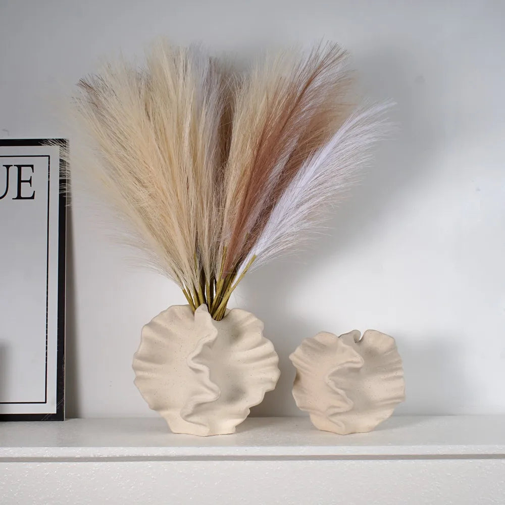 Decorative shell vases with dried pampas grass on a white surface.